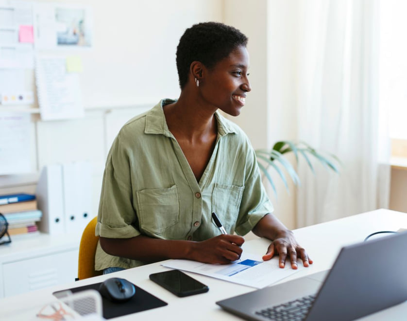 Smiling woman taking notes while looking at a laptop.