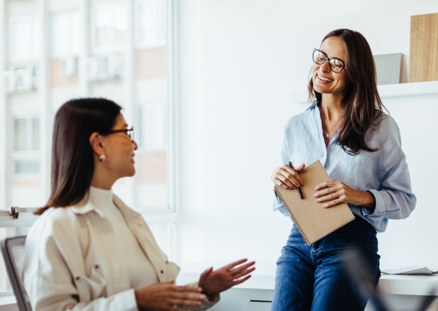 Two women workers smiling and working together in a contemporary office setting