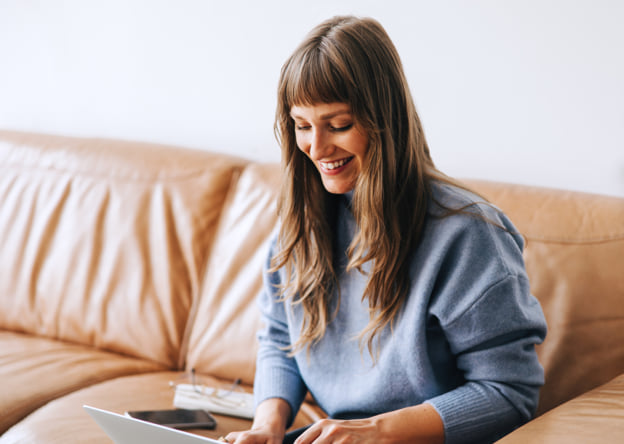 Woman sitting on a couch working on a laptop.