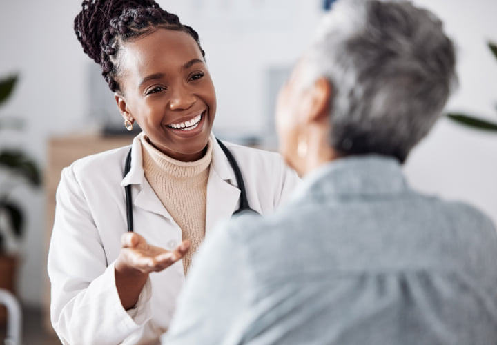 Health professional wearing a white coat and stethoscope smiling while chatting with a patient.