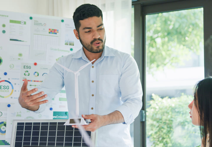 Man presenting a small-scale windmill. A colorful report is on display behind him.