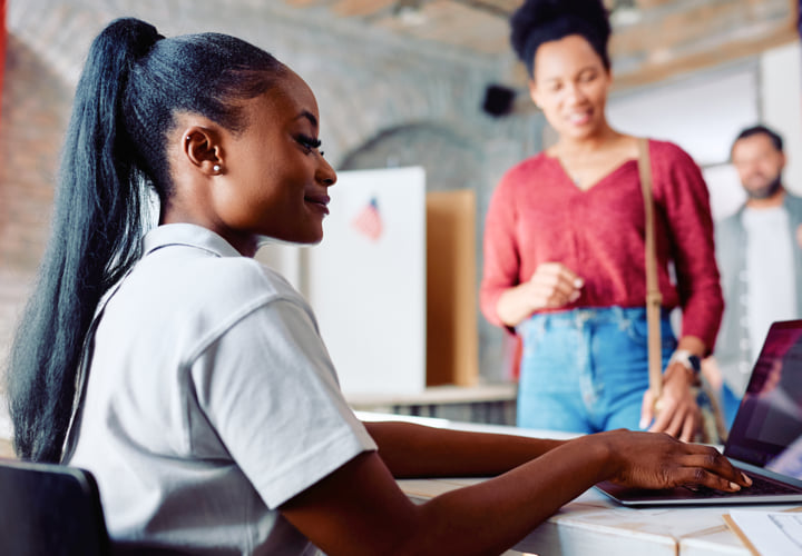Woman working at a laptop while two people are in line waiting to speak with her.