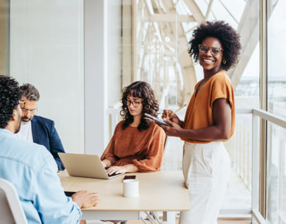 Woman standing while a group of coworkers work at their laptops.