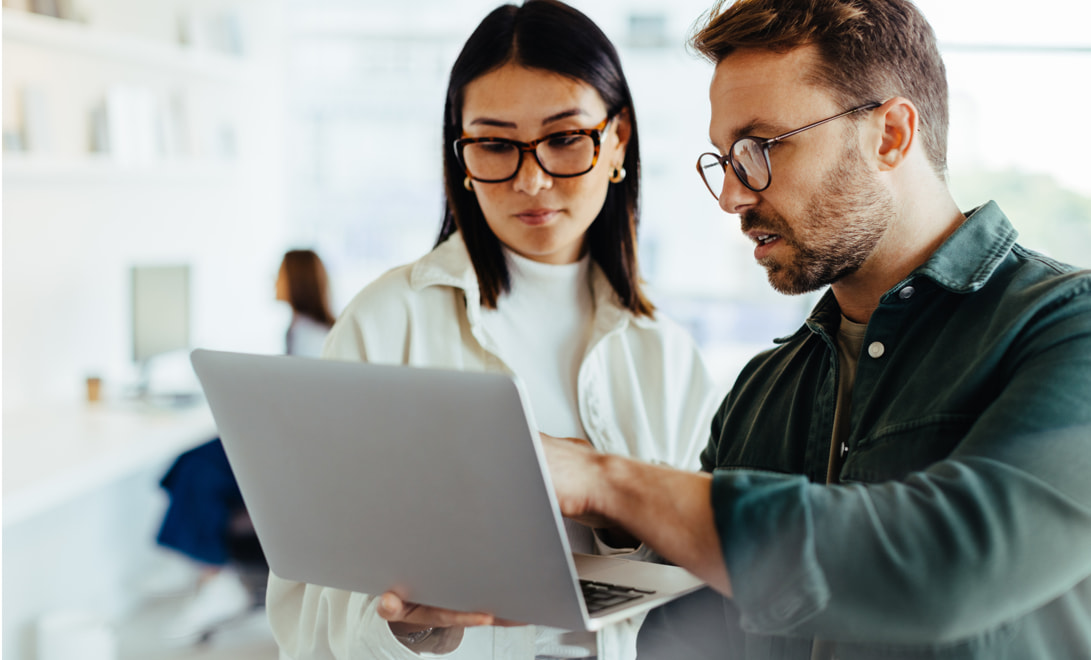 Two coworkers standing while reviewing something on a laptop.