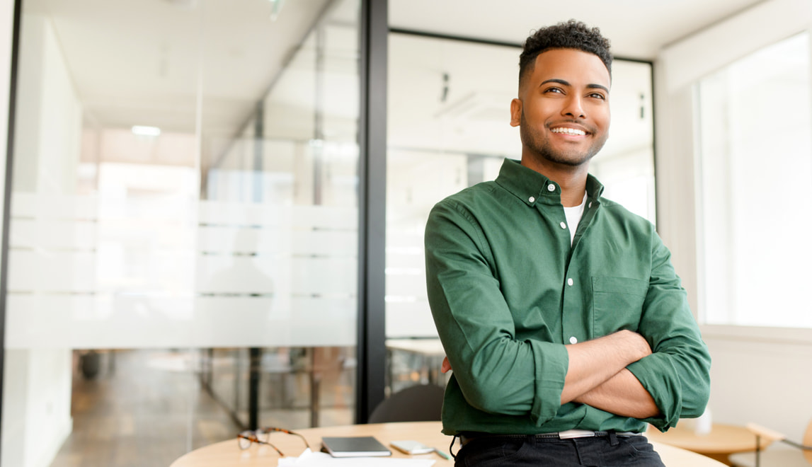 Man smiling with his arms folded in a contemporary office setting.