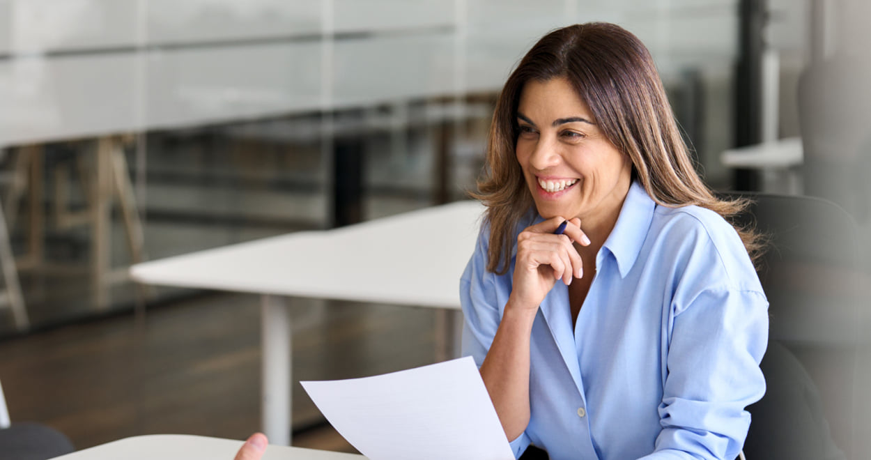 Woman smiling while holding a document in a bright office setting.