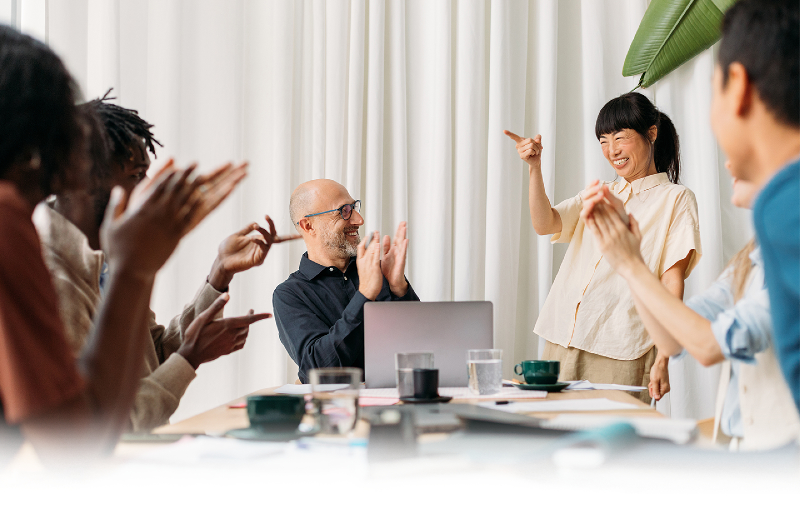 Group of coworkers clapping and smiling while the leader points at her team, with a red ‘Encourage the Heart’ banner at the bottom.
