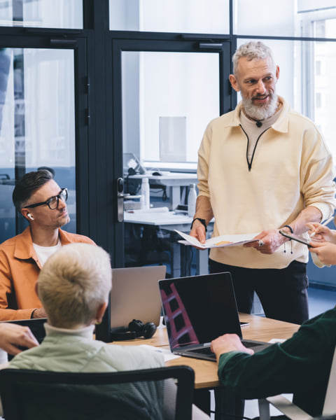 Man standing while coworkers listen to what he’s saying.