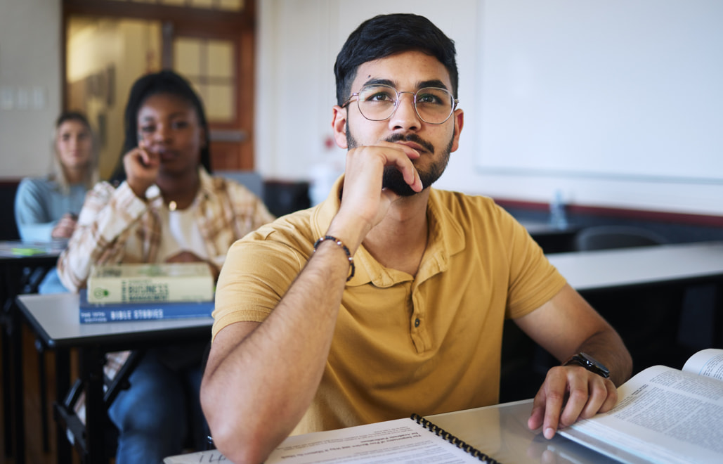 Young male student sitting at a desk in a classroom setting.