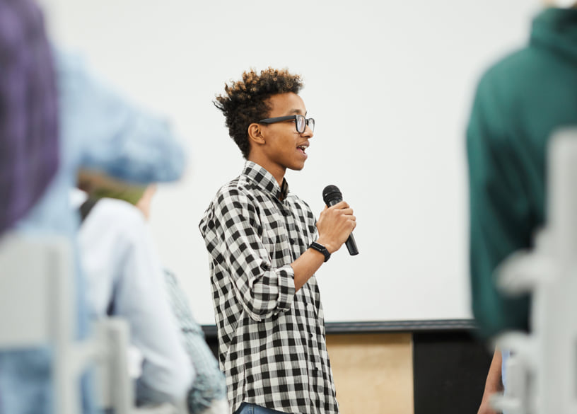 Young male student speaking in front of a crowd.