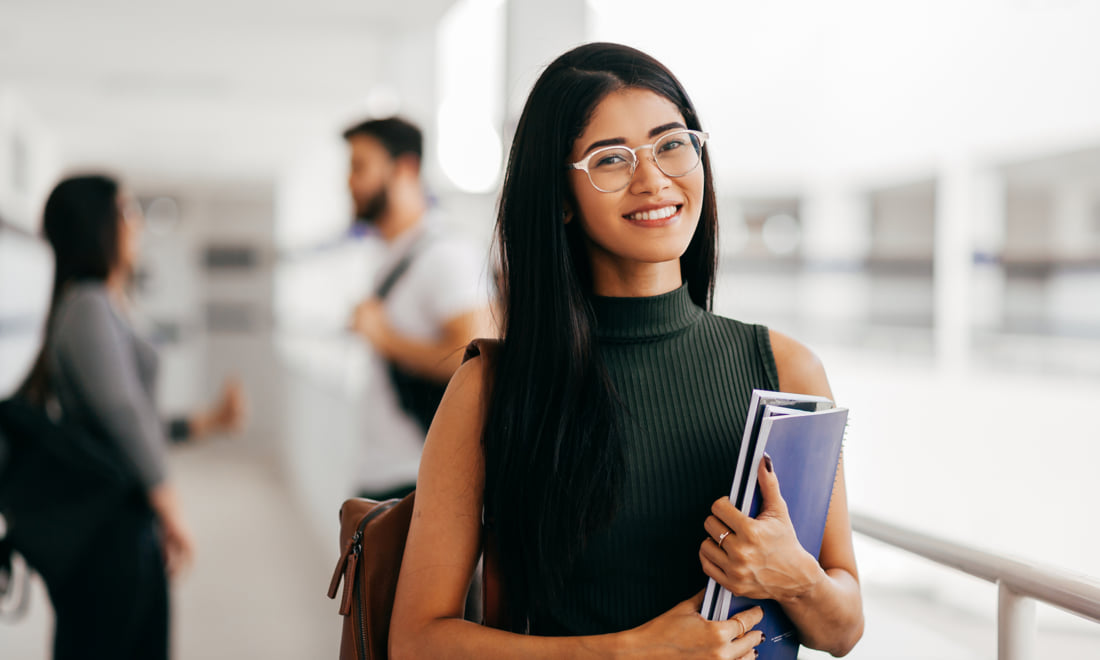 Young woman student smiling and holding notebooks in a university setting.