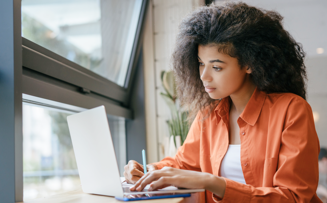 Woman writing in a notebook while looking at a laptop.