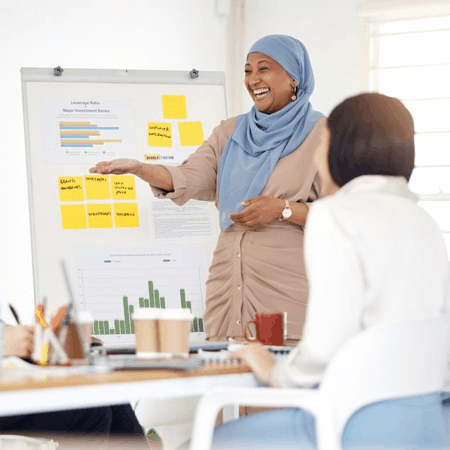 Woman smiling while presenting data from a board to a group of coworkers.