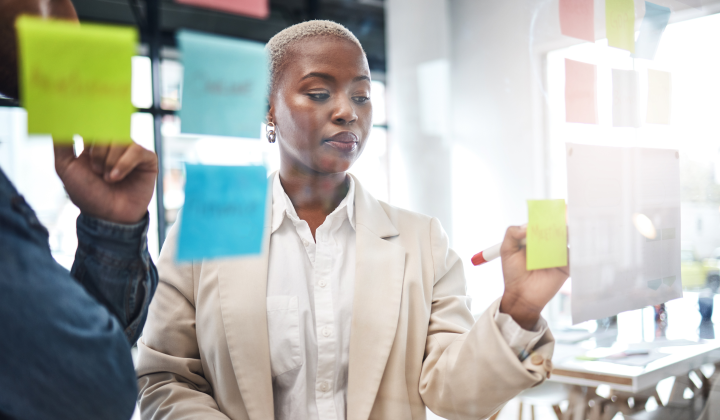 Woman writing on colorful sticky it notes in a bright office setting.