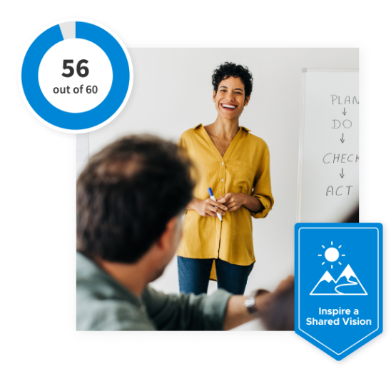 Smiling woman standing in front of a board with a blue ‘Inspire a Shared Vision’ banner at the bottom and a 56 out of 60 scale in the top left corner.